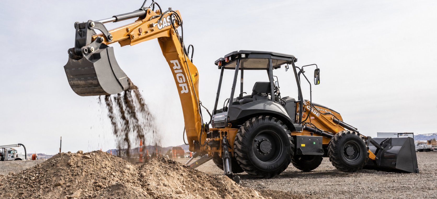 RIGR-branded CASE backhoe loader loading gravel at a job site